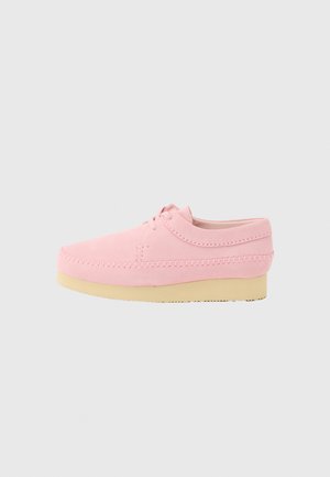 Roze suède casual schoen met beige crepezool, gestikte details en vetersluiting op een effen lichtgrijze achtergrond.
