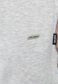 Grå sweatshirt med en blød tekstur, lille "SMILODOX" logo patch og en sort label på sidesømmen. Klassisk crew neck design.