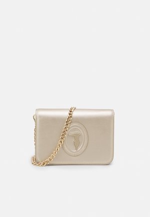 Sac bandoulière en cuir beige avec une sangle en chaîne dorée et un logo ovale embossé sur le rabat avant, présenté sur un fond uni.