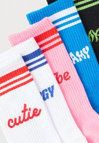 Πέντε πολύχρωμες ριμπ κάλτσες με ρίγες στην κορυφή, καθεμία με διαφορετική λέξη κεντημένη σε αντιθετικά χρώματα.