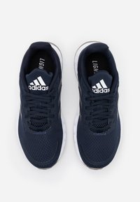 Ett par marinblå Adidas löparskor med vita sulor, svarta snören och Adidas-logotypen på tungan, sett ovanifrån på en vit bakgrund.