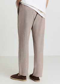 Hellbraune, locker sitzende Hose mit dezentem Schimmer, seitlichen Taschen und geradem Schnitt, kombiniert mit braunen Slippern.