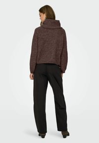 Brūna adīta džemperis ar plašu, rullētu apkakli un īsāku dizainu, kombinēts ar melniem platiem biksēm un papēžainām kurpēm.