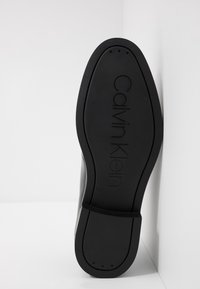 Semelle noire de chaussure Calvin Klein en matériau en caoutchouc texturé, présentant un logo de marque en relief et plusieurs trous de drainage pour une meilleure traction.