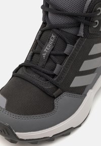 Schwarzer Wanderschuh mit einer strukturierten Mesh-Oberfläche, grauen Akzenten und einer verstärkten Zehenkappe. Mit gepolsterten Schnürsenkeln und einer robusten Sohle.