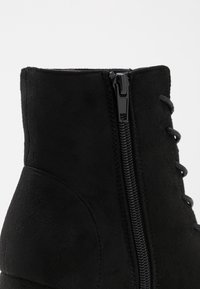 Stivale alla caviglia in suede nero con cerniera laterale e lacci, dalla texture liscia e con cavigliera imbottita per comfort e supporto.