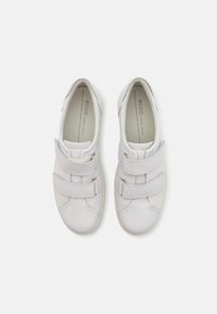 Ett par vita lädersneakers med dubbla kardborreband, texturerad yta och märkta vadderade innersulor, visade ovanifrån på vit bakgrund.