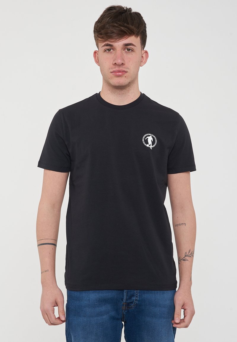 T-shirt nera in cotone concollo rotondo, con un piccolo logo bianco sul lato sinistro del petto e maniche corte. Indossata con jeans in denim blu.