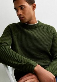 Jersey verde de punto con textura acanalada, cuello redondo y mangas largas. Presenta costuras raglán y una silueta ajustada.