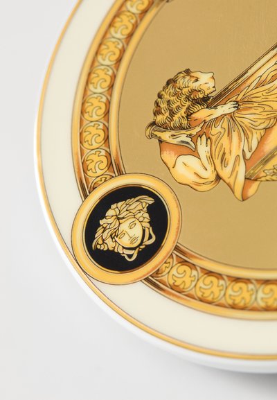 Arany háttérrel díszített dísztányér, finom oroszlán- és alakdíszítésekkel. Fekete kör alakú részlet arc motívummal. Elegáns porcelán kivitel.