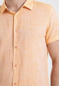 Chemise à manches courtes, boutonée, en tissu léger et texturé dans une teinte orange clair avec un motif rayé subtil.