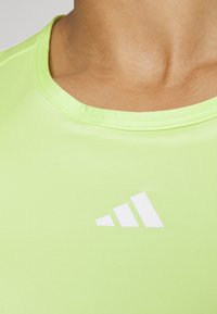 Lichtgroen sportshirt met een ronde halslijn en een gladde textuur. Voorzien van een wit Adidas-logo aan de voorkant, nabij de schouder.