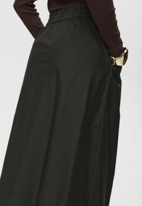 Jupe noire taille haute en tissu léger avec une taille élastique froncée et des poches latérales, présentant un design lisse et fluide.