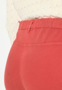 Pantalones rojos de cintura elástica con una textura suave y detalles de costura. Llevados con un suéter de punto texturizado de color claro.