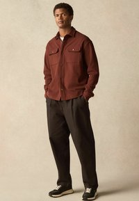 Marron knap-op skjorte med to brystlommer, parret med løse sorte bukser og sorte sneakers med cremefarvede detaljer.