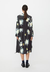 Czarna sukienka w kwiaty z długimi rękawami, elastyczną talią i marszczonym dołem. Ozdobiona dużymi żółtymi i niebieskimi kwiatowymi wzorami. Noszona z czarnymi butami.
