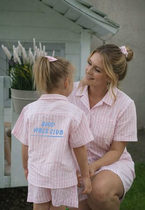 Mother kneeling and smiling at young girl in matching pink striped outfits, girl’s shirt reads “GOOD VIBES CLUB” in blue text.