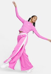 Rozā sporta komplekts, kas sastāv no īsa garām piedurknēm topa un platām biksēm ar baltām sānu svītrām un rāvējslēdzējiem. Materiāls izskatās gluds un elastīgs.