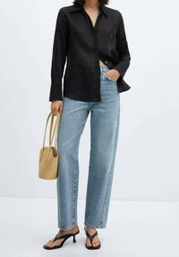 Camisa de lino negra de botón, jeans de pierna ancha azul claro, chanclas negras y un pequeño bolso de cubo beige. Conjunto simple y casual.
