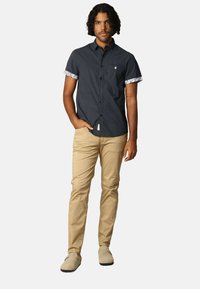 Korte mouwen, marineblauw gestreept shirt met witte bloemenmanchetten, gecombineerd met beige chinos. Model draagt lichtgekleurde schoenen.