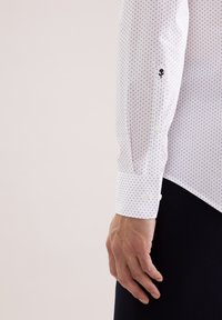 Biała koszula z długim rękawem w niebieskie groszki, z mankietami na guziki i haftowanym kwiatowym akcentem na rękawie.