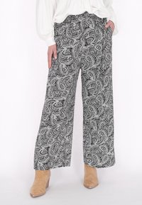 Pantaloni a gamba larga in bianco e nero a motivo paisley, con una texture morbida, dotati di vita alta e tasche laterali, abbinati a stivali alla caviglia beige.