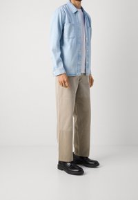 Light blue denim shirt with button closure and two chest pockets, paired with beige wide-leg trousers and black lace-up shoes.