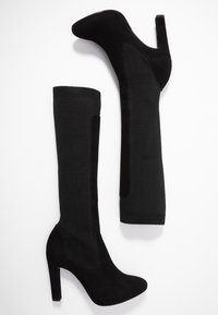 Bottines noires montantes en suède lisse et tissu côtelé, dotées d'une forme fuselée et d'un talon bloc haut.