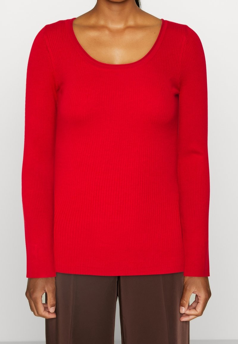 Rotes, geripptes Langarmoberteil mit U-Boot-Ausschnitt; figurbetontes Design und glatte Textur; kombiniert mit braunen Hose mit weitem Bein.