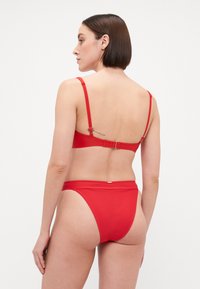 Punainen bikinit setti, jossa on säädettävät hihnat, nyöri takana ja sileä kangas, jossa on minimaalinen ommel. Alhaalla oleva osa on matala vyötärö, jossa on saumatonta muotoilua.