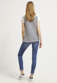 Raidallinen t-paita pyöreällä pääntiellä ja pitsisillä lyhyillä hihoilla, yhdistettyinä tiukkoihin sinisiin farkkuihin ja musta-valkoisiin urheilukukkiin.