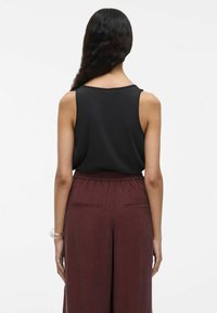 Zwart mouwloos topje gecombineerd met bordeaux brede broek. Het topje heeft een ronde halslijn en een gladde textuur. De broek heeft een elastische tailleband en zijzakken.