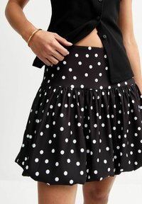 Jupe noire à pois blancs avec un ourlet froncé et une large taille. Fabriquée dans un tissu à texture lisse. Les pois blancs contrastent avec le noir.