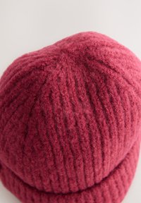 Strickmütze in tiefem Rot mit geripptem Muster und umgeschlagenem Rand. Weicher Stoff mit sichtbaren Fasern sorgt für Wärme.