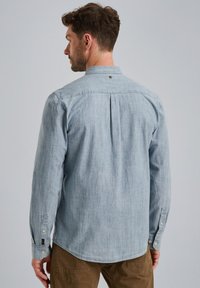 Camisa de manga larga azul claro hecha de tejido chambray, con un pliegue en la parte posterior, puños con botón y cuello. Textura sutil con líneas limpias.