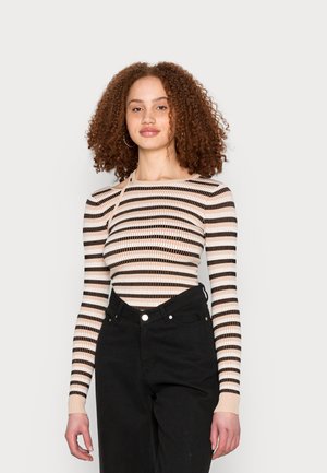 Camisola de manga longa com riscas horizontais em bege, castanho e creme. Design justo com textura canelada e decote barco. Combinada com jeans pretos.