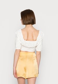 Top cropped branco com decote de babado em renda florida, combinado com calções amarelos de seda com uma textura suave e ajuste descontraído.
