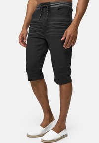 Pantalones cortos negros de mezclilla con cintura elástica y cordón. Presentan pliegues en la parte frontal y terminan justo por debajo de la rodilla.