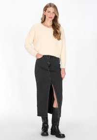 Krém színű, bordás kötésű pulóver hosszú ujjal. Magas derekú fekete farmer szoknya elöl sliccel. A modellen térdig érő fekete csizma van.