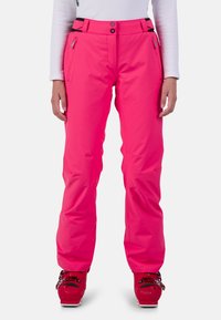 Rosa skidbyxor med rak skärning, utrustade med en zippered ficka och justerbar midja, kombinerade med röda skidstövlar.