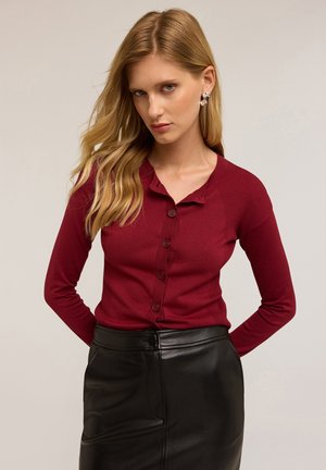 Cardigan bordeaux à manches longues avec un motif texturé, doté d'une fermeture à boutons et d'un col rond, associé à une jupe crayon en cuir noir.