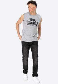 Gray sleeveless t-shirt featuring a black lion logo and "Lonsdale London" text, paired with black jeans and white sneakers.