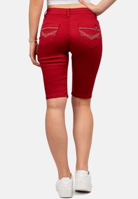 Bermuda shorts in denim rosso con una vestibilità slim, vita medio-alta e due tasche posteriori con cuciture decorative. Indossati con sneakers bianche.