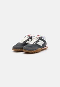Zapatillas deportivas grises con acentos blancos, con un upper de ante texturizado y una suela de goma color caramelo. Los cordones son de color crema y cuentan con un logo en la lengüeta.