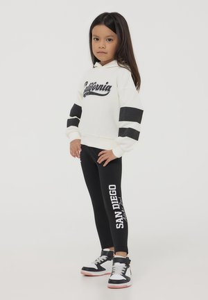 Felpa bianca con scritta 'California', maniche a righe nere, abbinata a leggings neri con stampa 'SAN DIEGO' e sneakers nere.