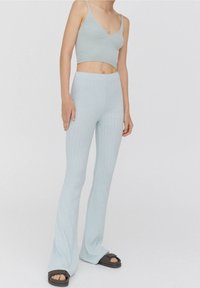 Haut court côtelé bleu clair et pantalon évasé, fabriqués en tissu doux. La tenue comprend des bretelles fines et une coupe ajustée, associée à des sandales foncées.
