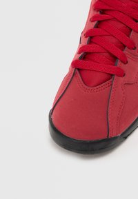 Zbliżenie czerwonego trampka z czerwonymi sznurowadłami i czarną podeszwą na białym tle.