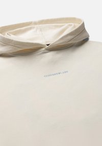 Crèmekleurige hoodie met het woord "TOMORROWLAND" geborduurd in kleine, lichtblauwe letters op de borst onder de capuchon.