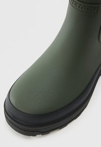 Stivale di gomma verde scuro con una superficie liscia, punta arrotondata e suola nera. Include un dettaglio di branding vicino alla parte superiore.