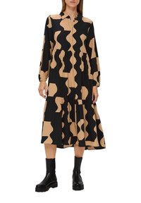 Abito a maniche lunghe con un motivo astratto in bianco e nero, chiusura con bottoni sul davanti, vita plissettata e gonna fluida. Abbinato a stivaletti neri.